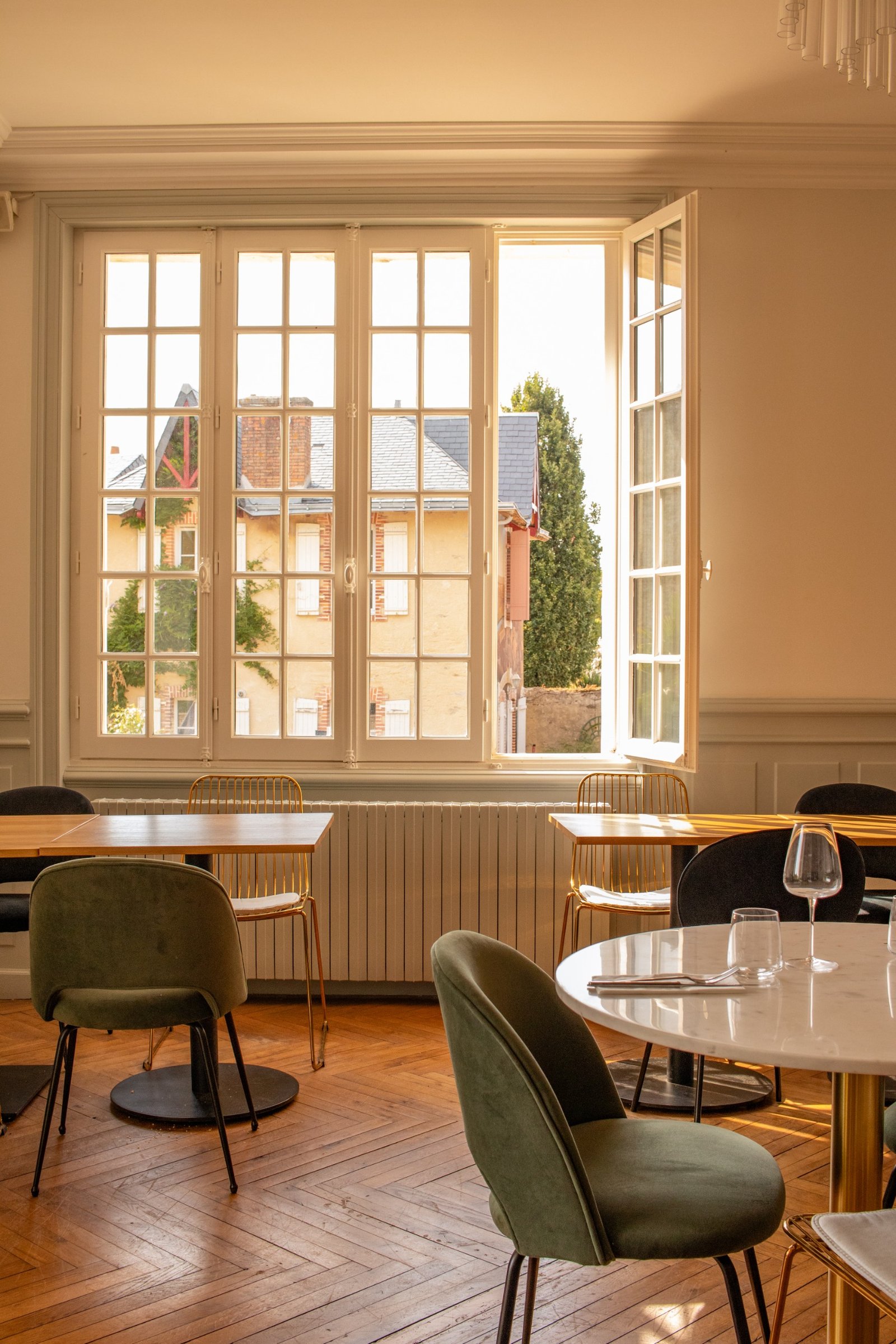 Restaurant interior in warm natural light with green velvet chairs and parquet flooring