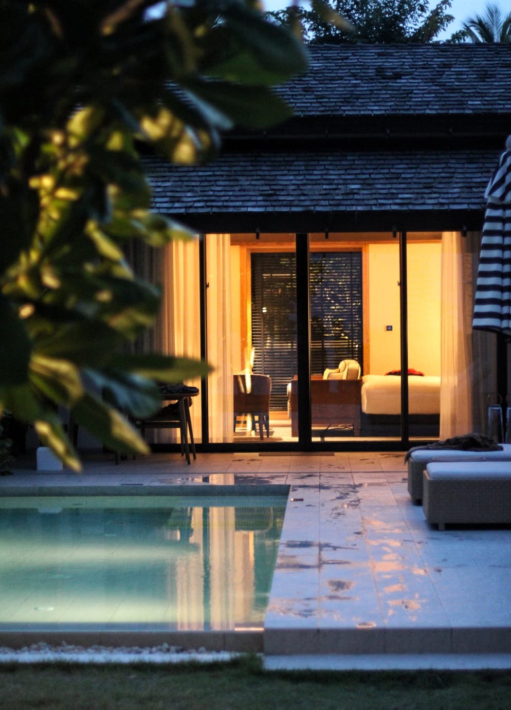 Tropical villa at dusk with warm interior light glowing across a private pool