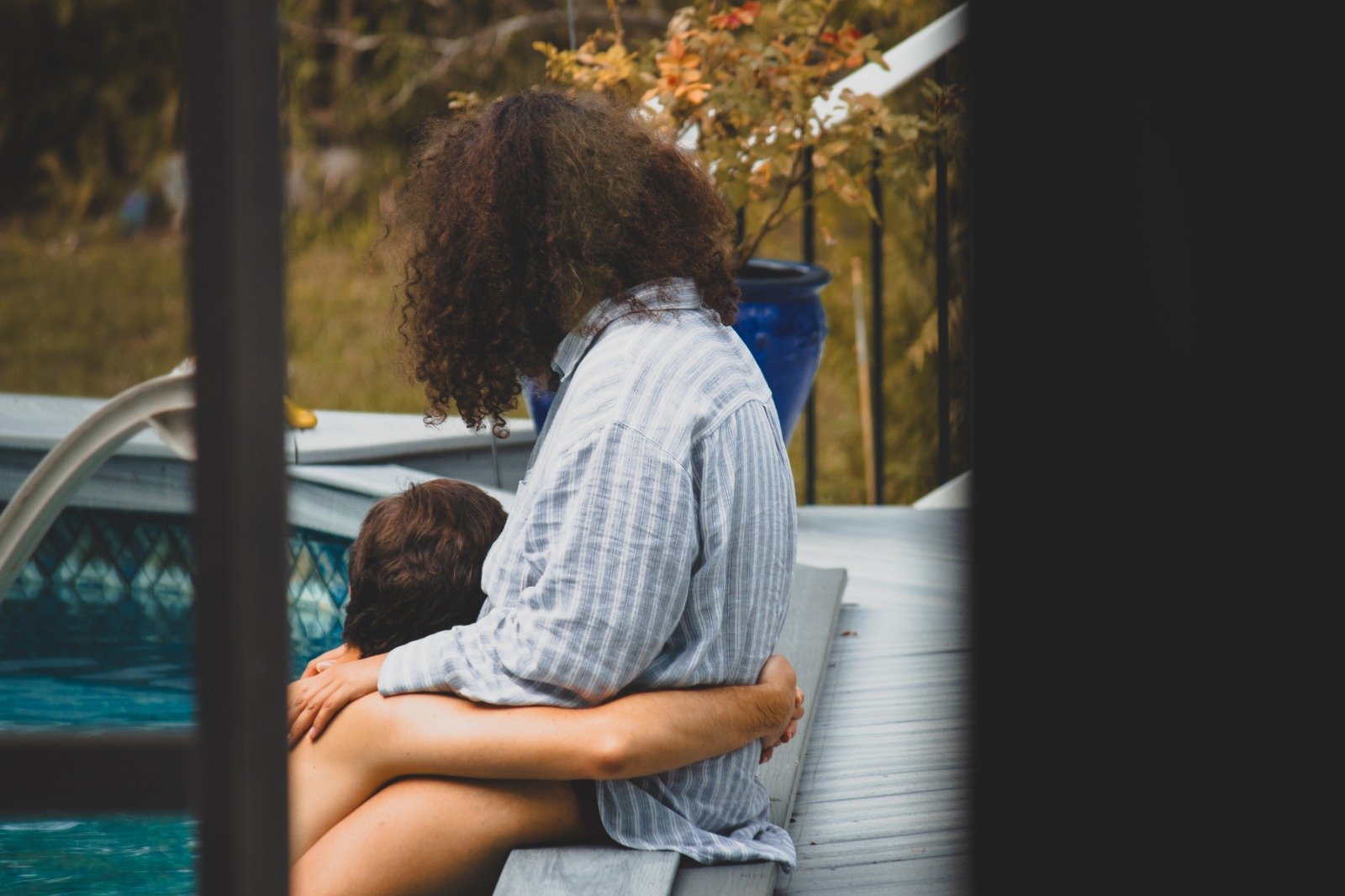 Couple sharing a quiet moment beside a swimming pool, seen through dark architectural framing