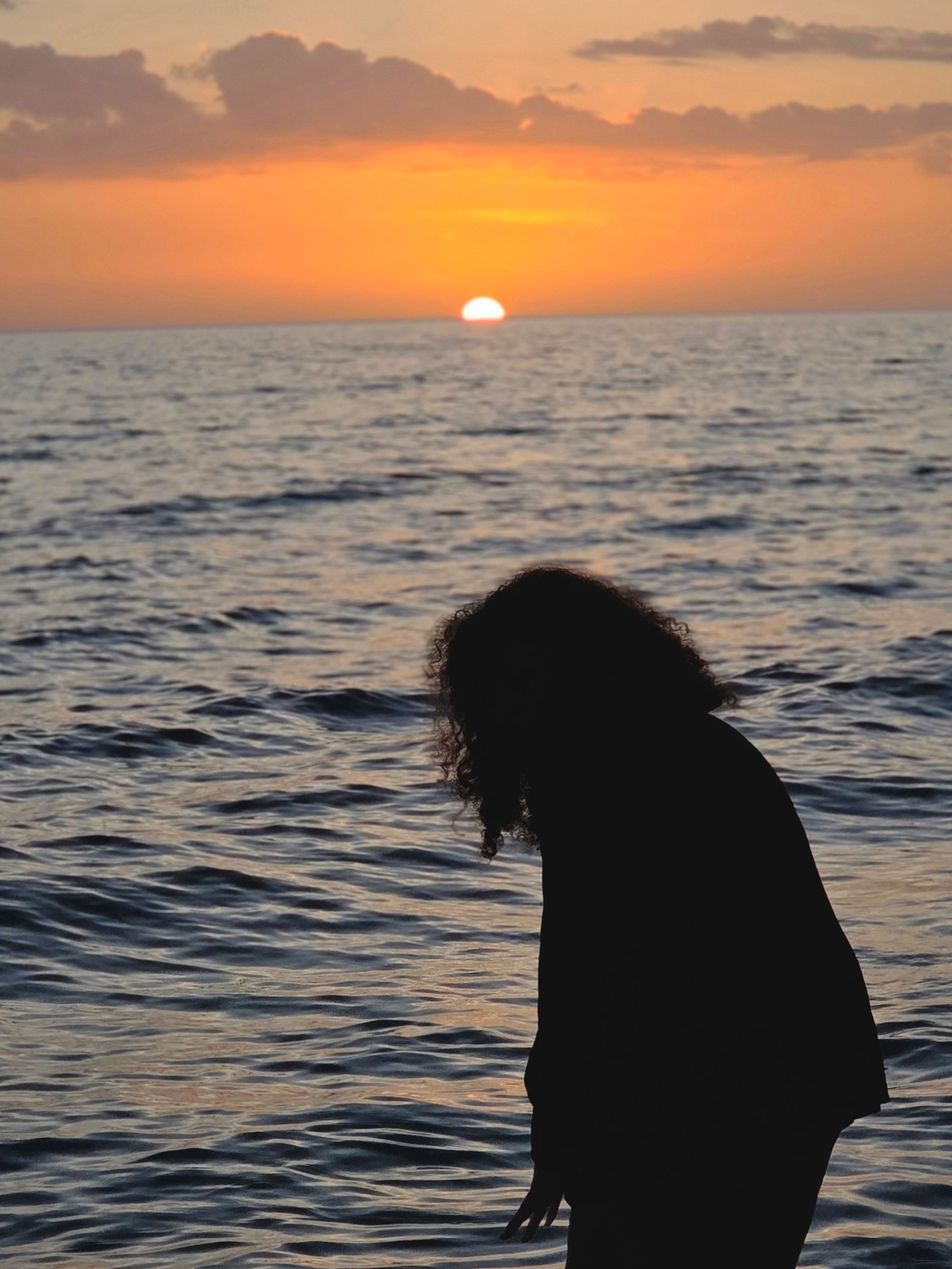 Silhouette of a woman by the sea as the sun sets on the horizon