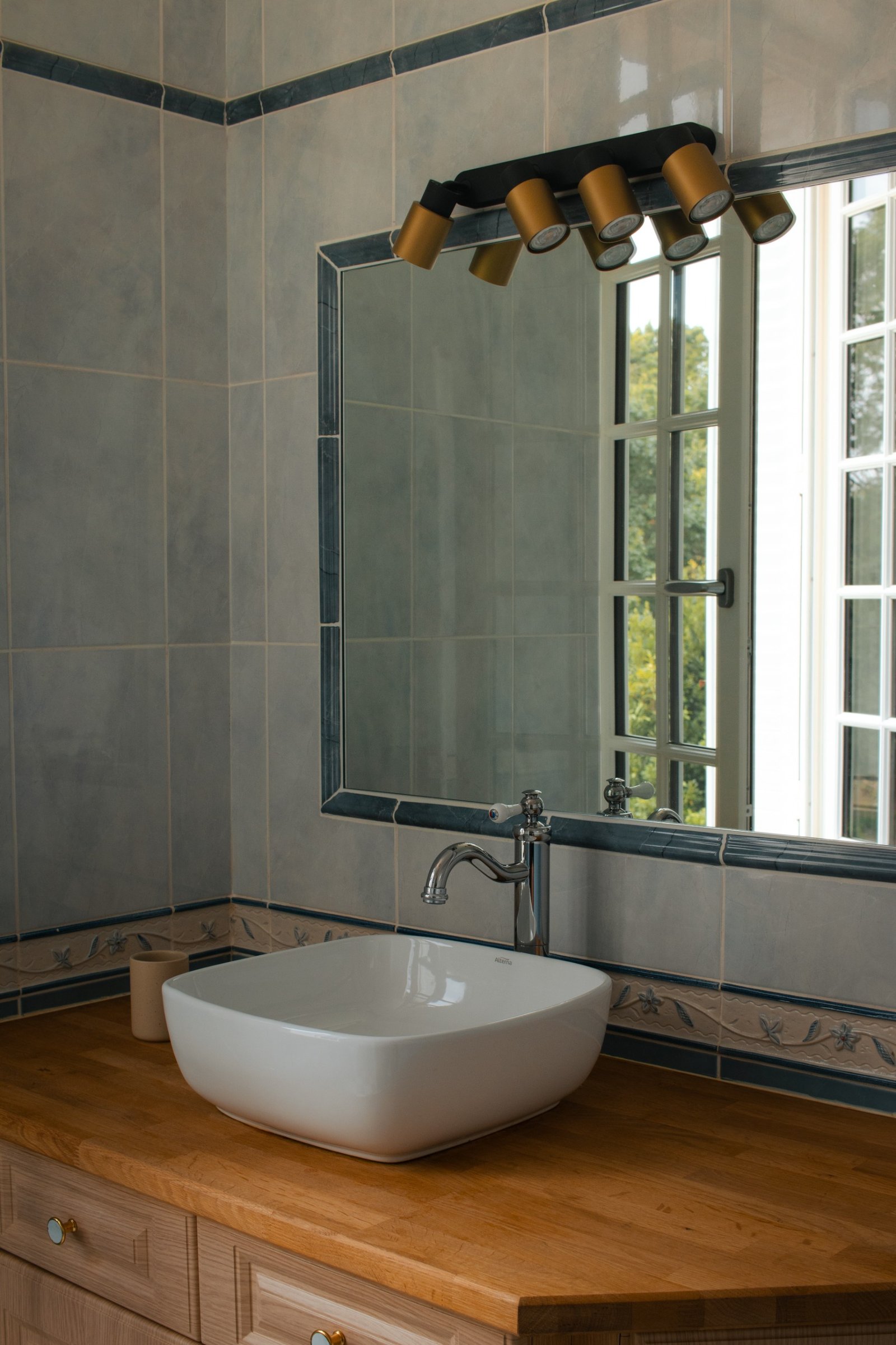 White basin on a wooden vanity with a mirror reflecting greenery