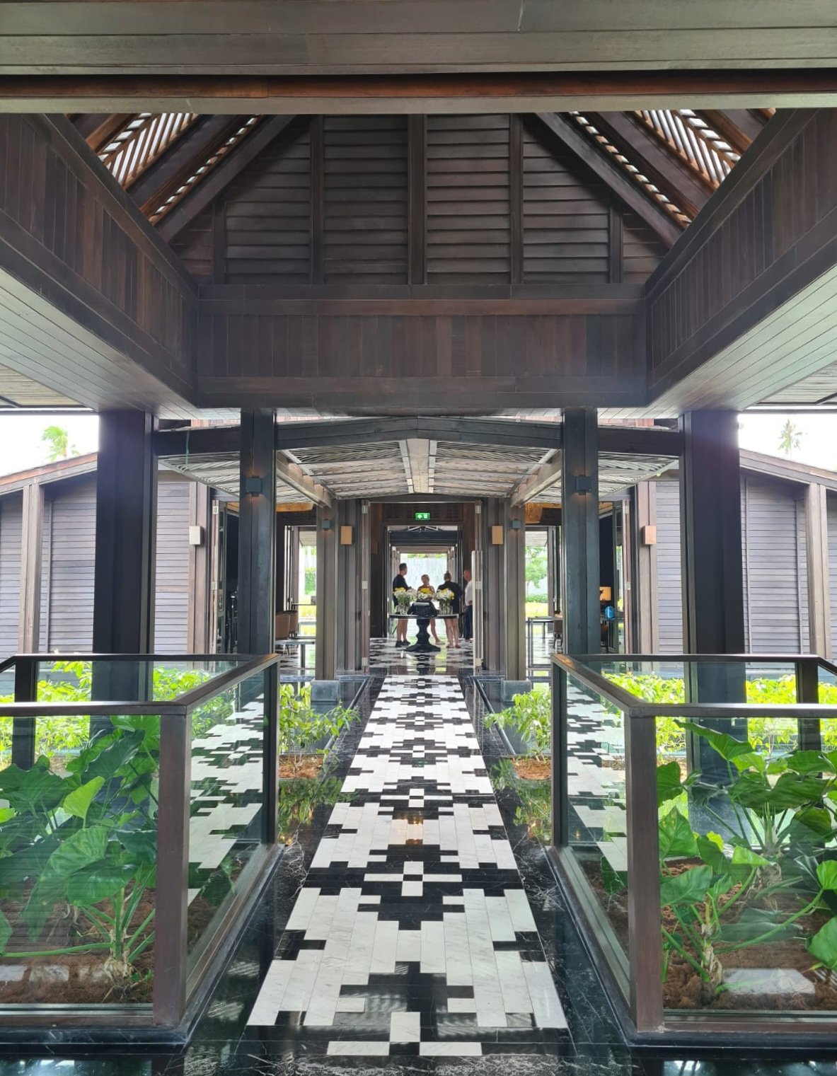 Timber pavilion walkway with a patterned mosaic path leading toward the light
